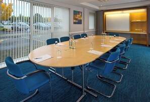 Ein Konferenzraum mit einem großen ovalen Tisch, blauen Stühlen und einer Projektionsleinwand.