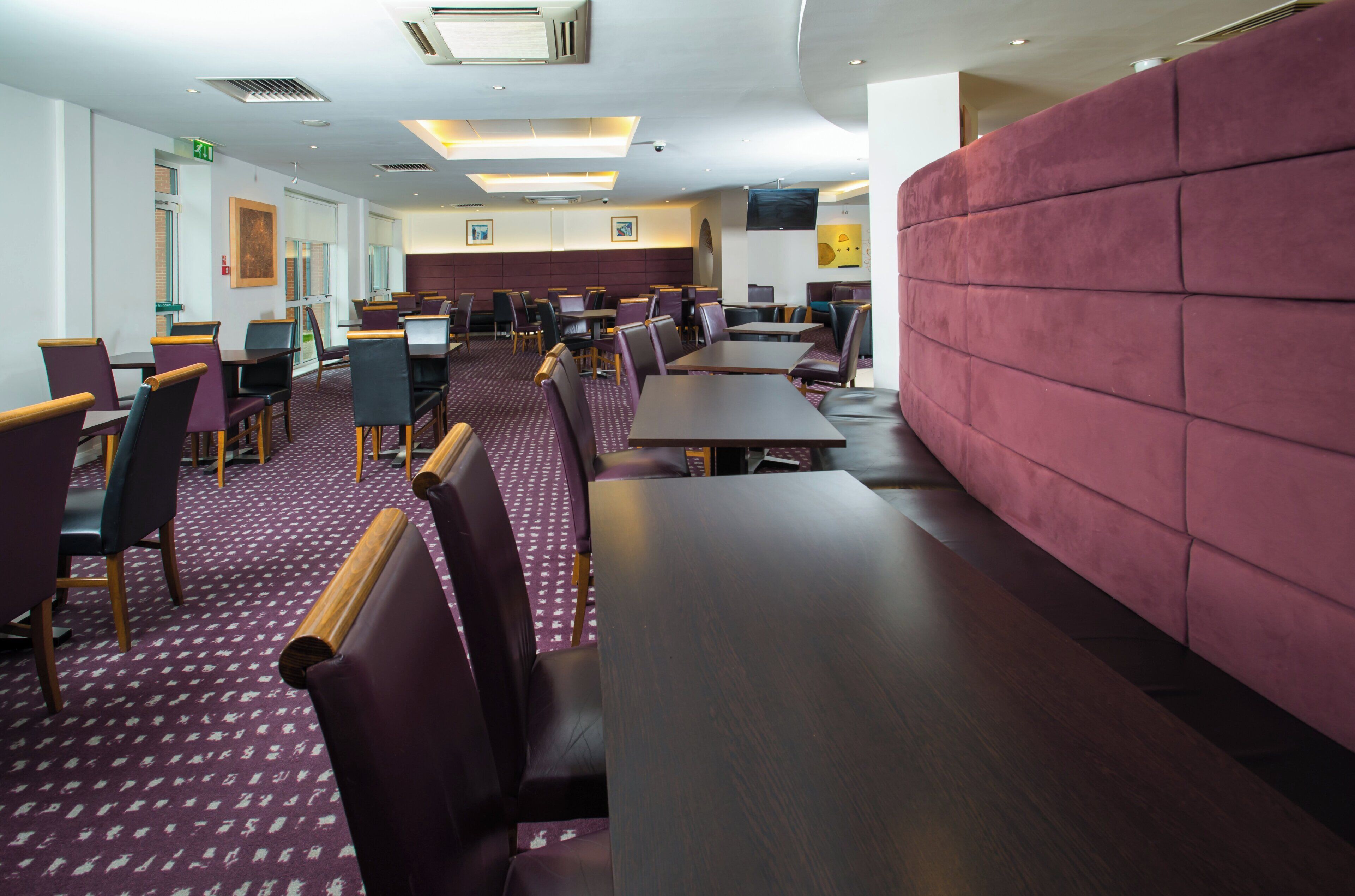 A restaurant with multiple tables and chairs, a patterned carpet, and a red cushioned wall.