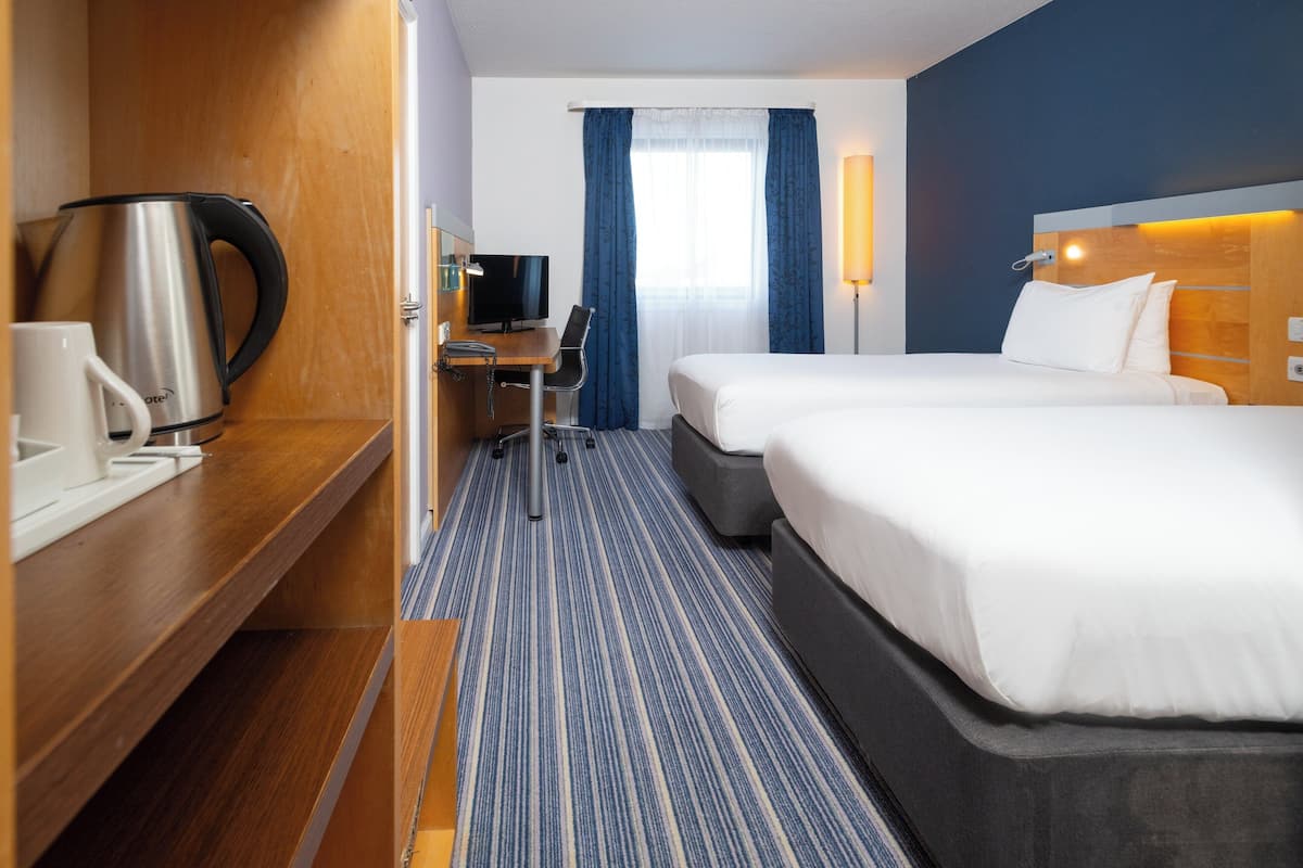Habitación de hotel con dos camas, un escritorio con silla, cafetera y televisión.