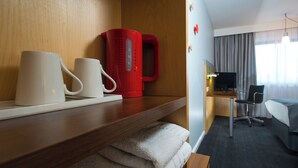 A hotel room with a wooden shelf holding two white mugs, a red coffee maker, and a folded towel. - Holiday Inn Express Bedford by IHG (Bedford)
