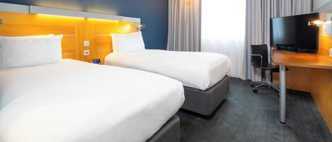 A hotel room with two beds, a desk with a TV, and a large window with curtains.