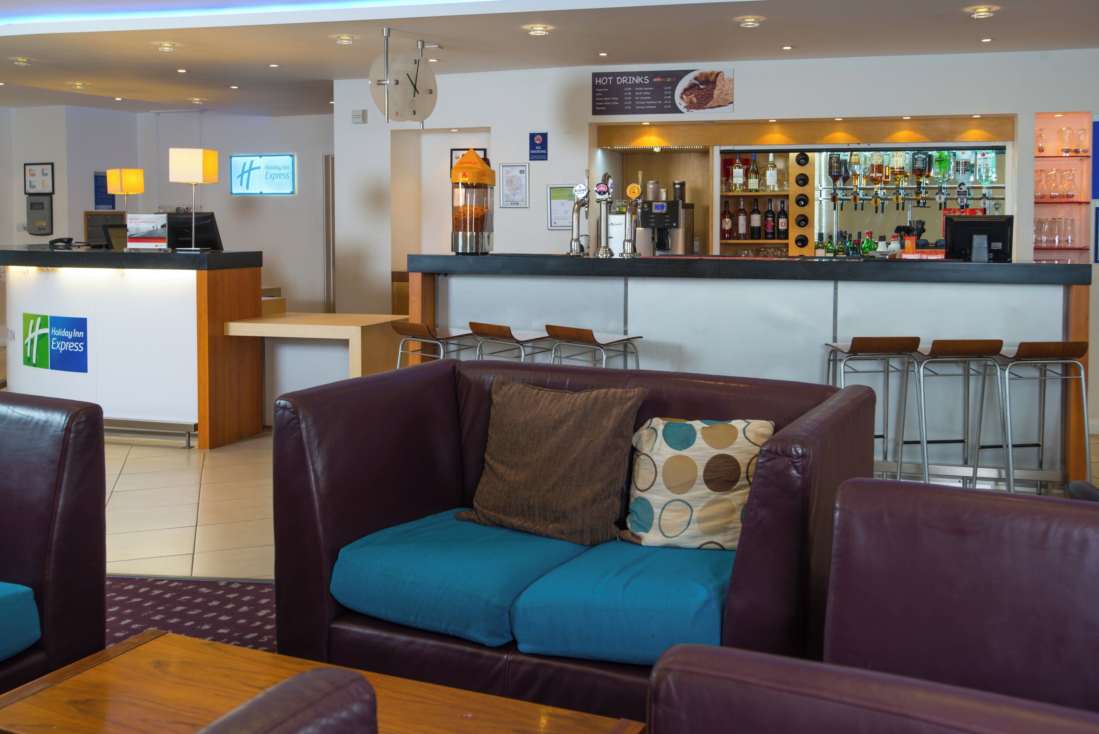 Een hotel lobby met een receptiebalie, een bar en zithoekjes, waaronder een bank en stoelen.