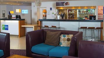 A hotel lobby with a reception desk, a bar area, and seating arrangements including a sofa and chairs.