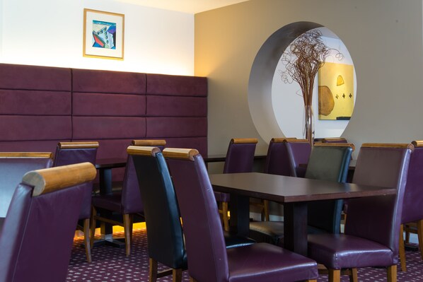 A restaurant with purple upholstered booths and wooden tables. - Holiday Inn Express Bedford by IHG (Bedford)