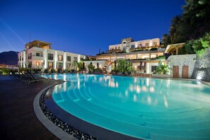 A large, curved swimming pool with a wooden deck and lounge chairs, surrounded by modern buildings with balconies and outdoor seating areas. - Ramada Resort by Wyndham Bodrum (Bodrum)