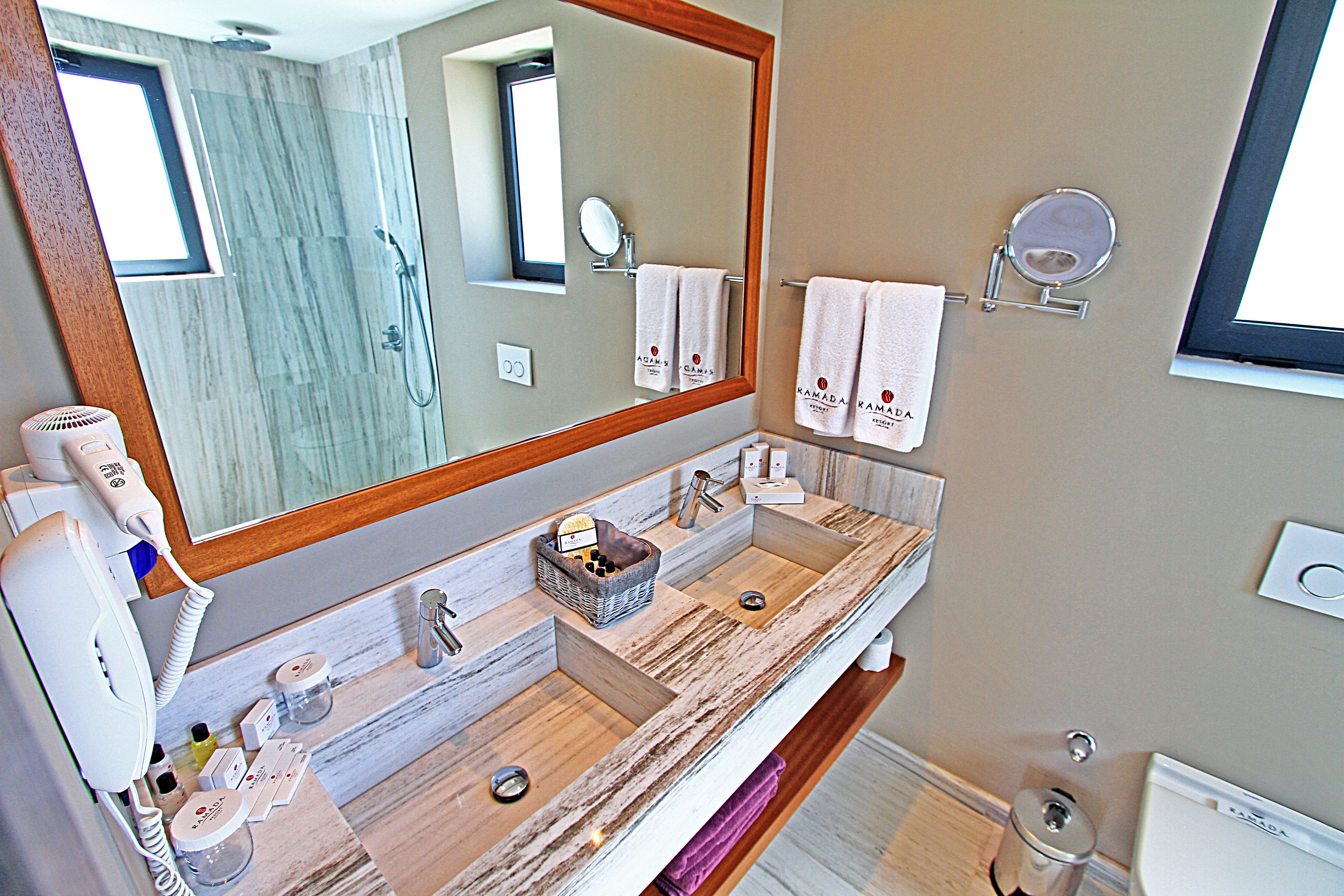 A modern bathroom with a large mirror, two sinks, a hairdryer, and a towel rack with towels.
