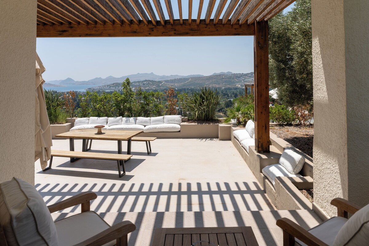 Un patio al aire libre con una pérgola de madera, un conjunto de sofás y una mesa de comedor.
