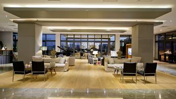 Un vestíbulo amplio con techo alto, ventanas grandes y una zona de estar central con sofás y sillones.