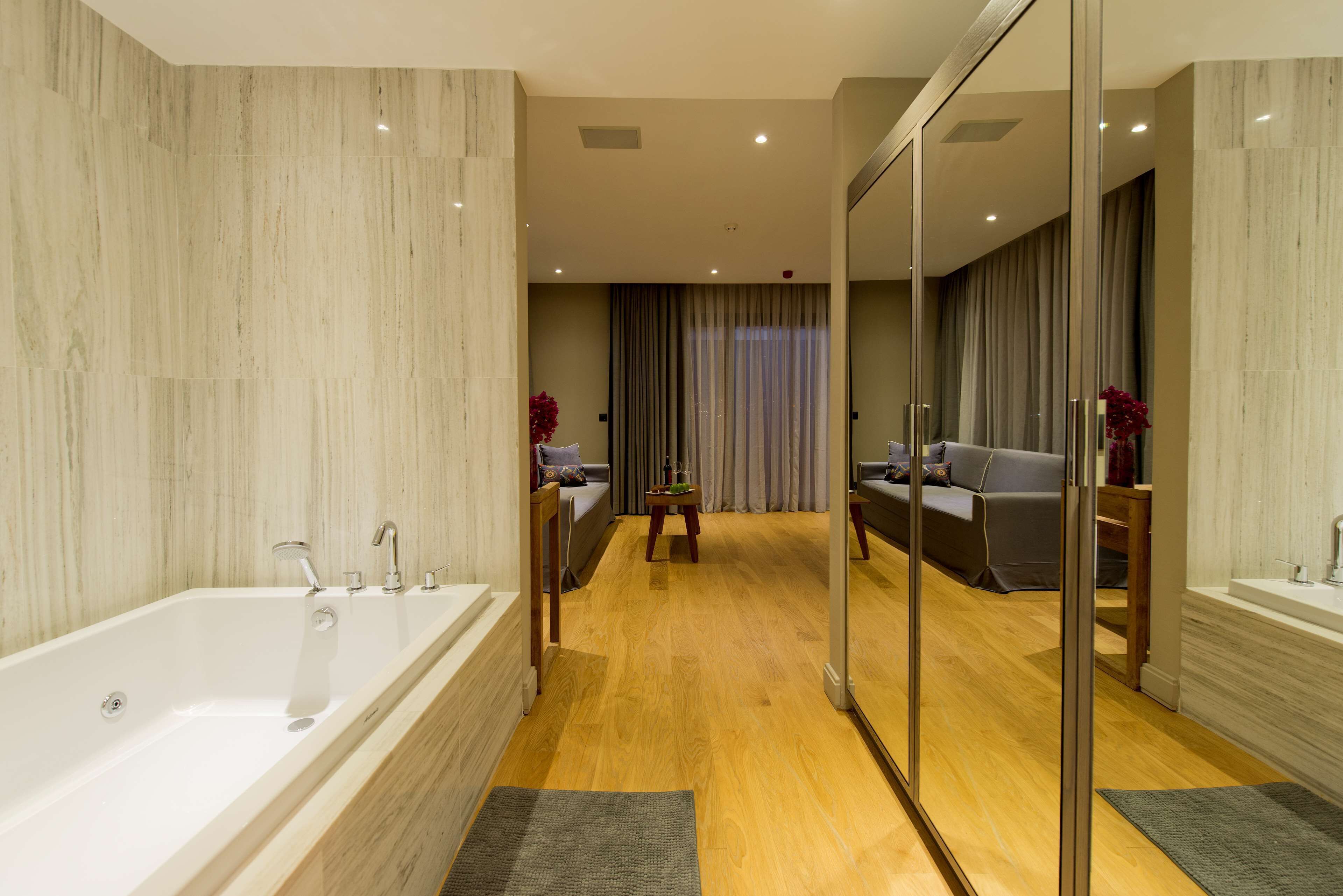 A modern bathroom with a large bathtub, wooden flooring, and a glass shower enclosure.