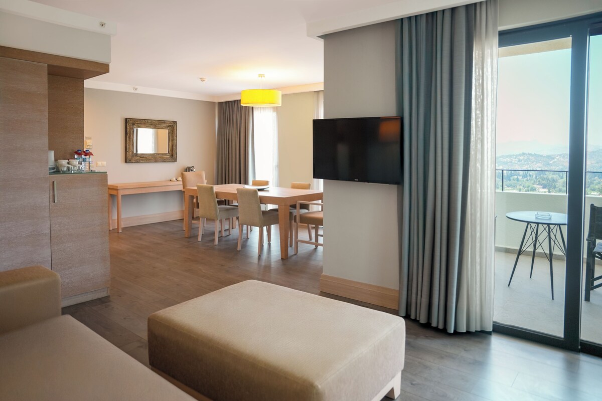 Habitación de hotel con comedor, televisor montado en la pared y balcón con vistas.