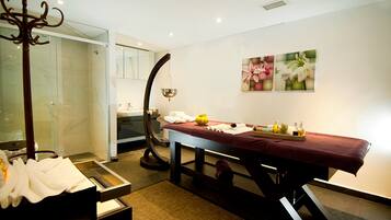 Un cuarto de spa con una camilla de masaje, cabina de ducha de vidrio y una pared decorada con motivos florales.
