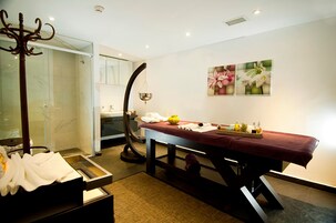 Un cuarto de spa con una camilla de masaje, cabina de ducha de vidrio y una pared decorada con motivos florales.