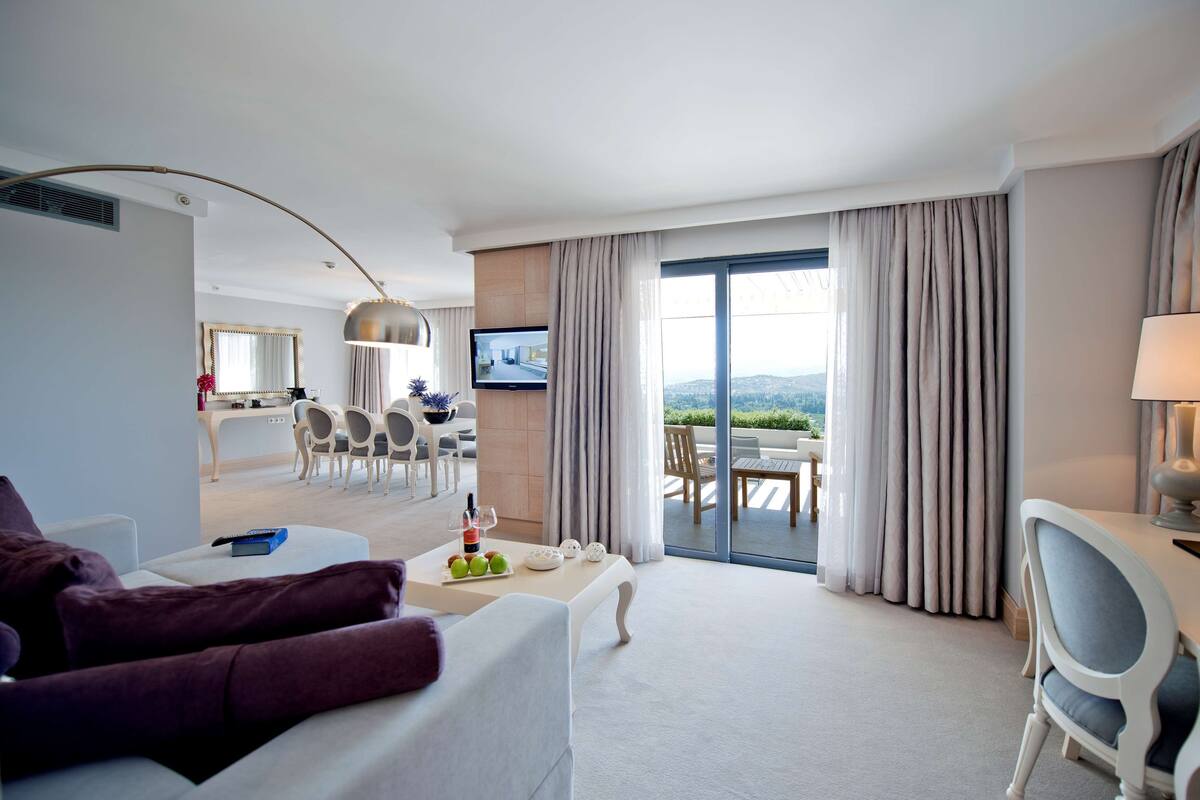 Habitación de hotel con balcón, zona de comedor y televisor.