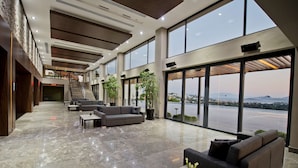 A spacious lobby with a marble floor, large windows offering a view of a body of water and distant hills, and a staircase leading to upper levels. - Ramada Resort by Wyndham Bodrum (Bodrum)