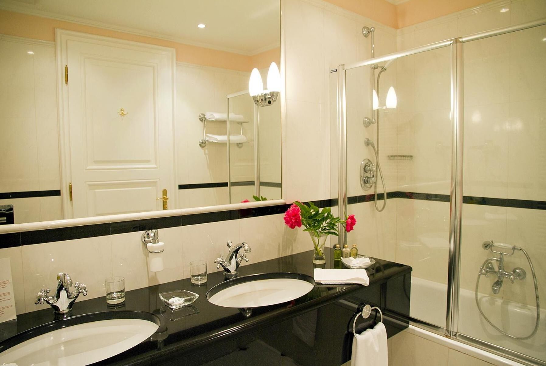 Een moderne badkamer met twee wasbakken, een grote spiegel en een douche met glazen wanden.