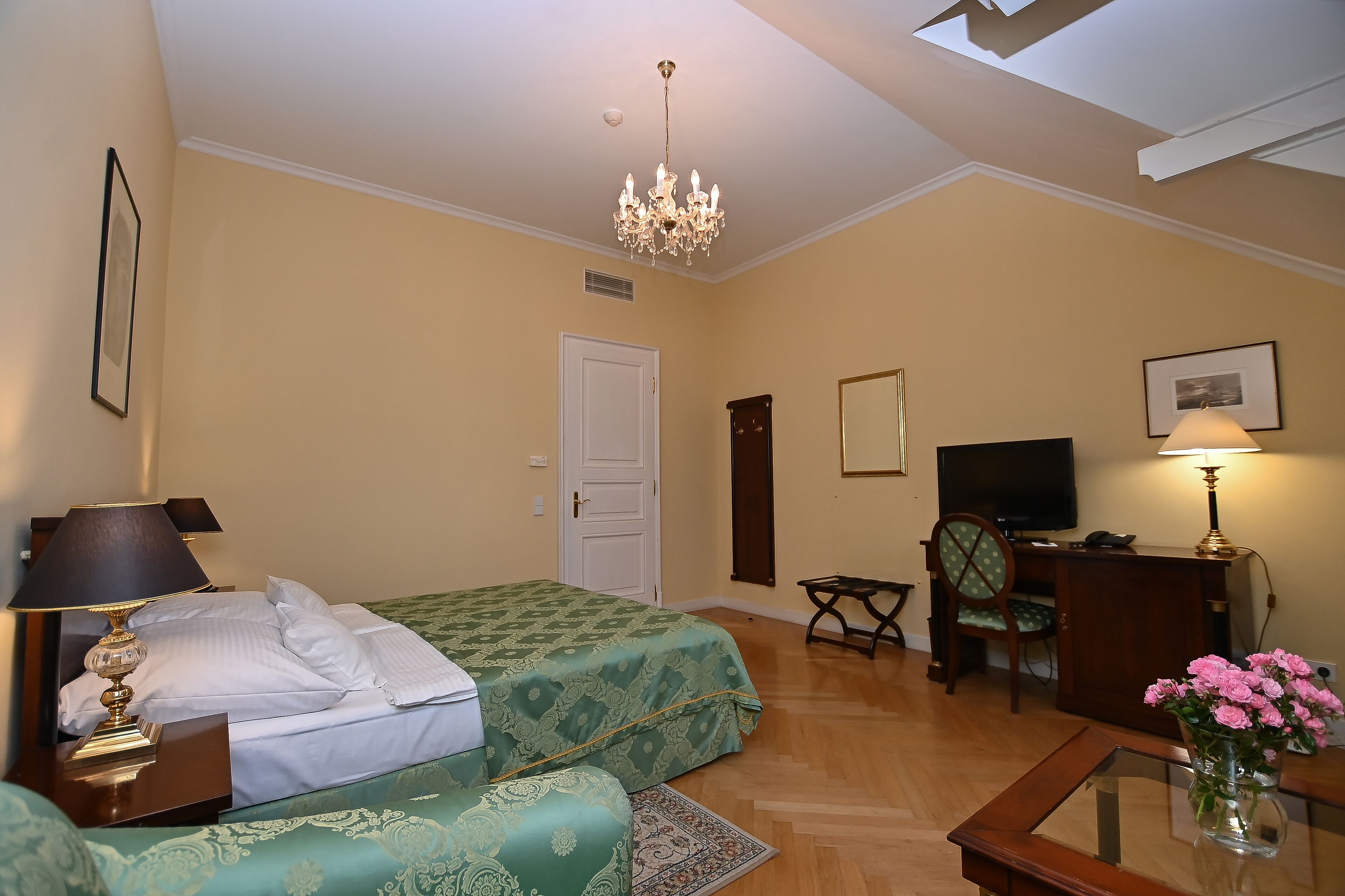 A hotel room with two beds, a desk, a TV, and a chandelier.