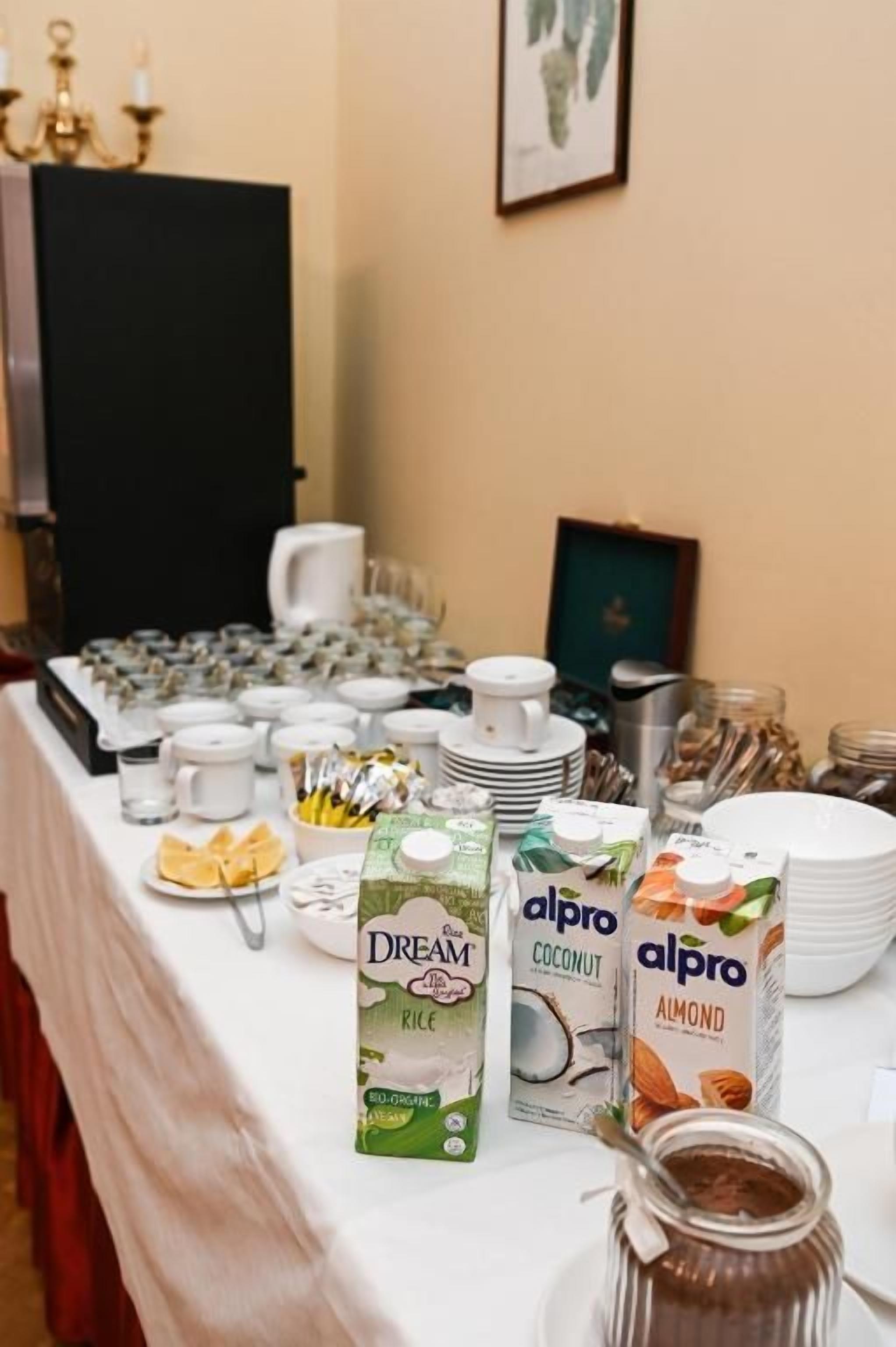 A buffet table with various food items and beverages, including cartons of almond and coconut milk, and a jar of jam.