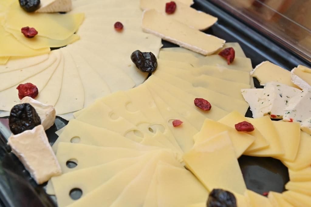 A variety of cheese and dried fruits displayed in a refrigerated case.