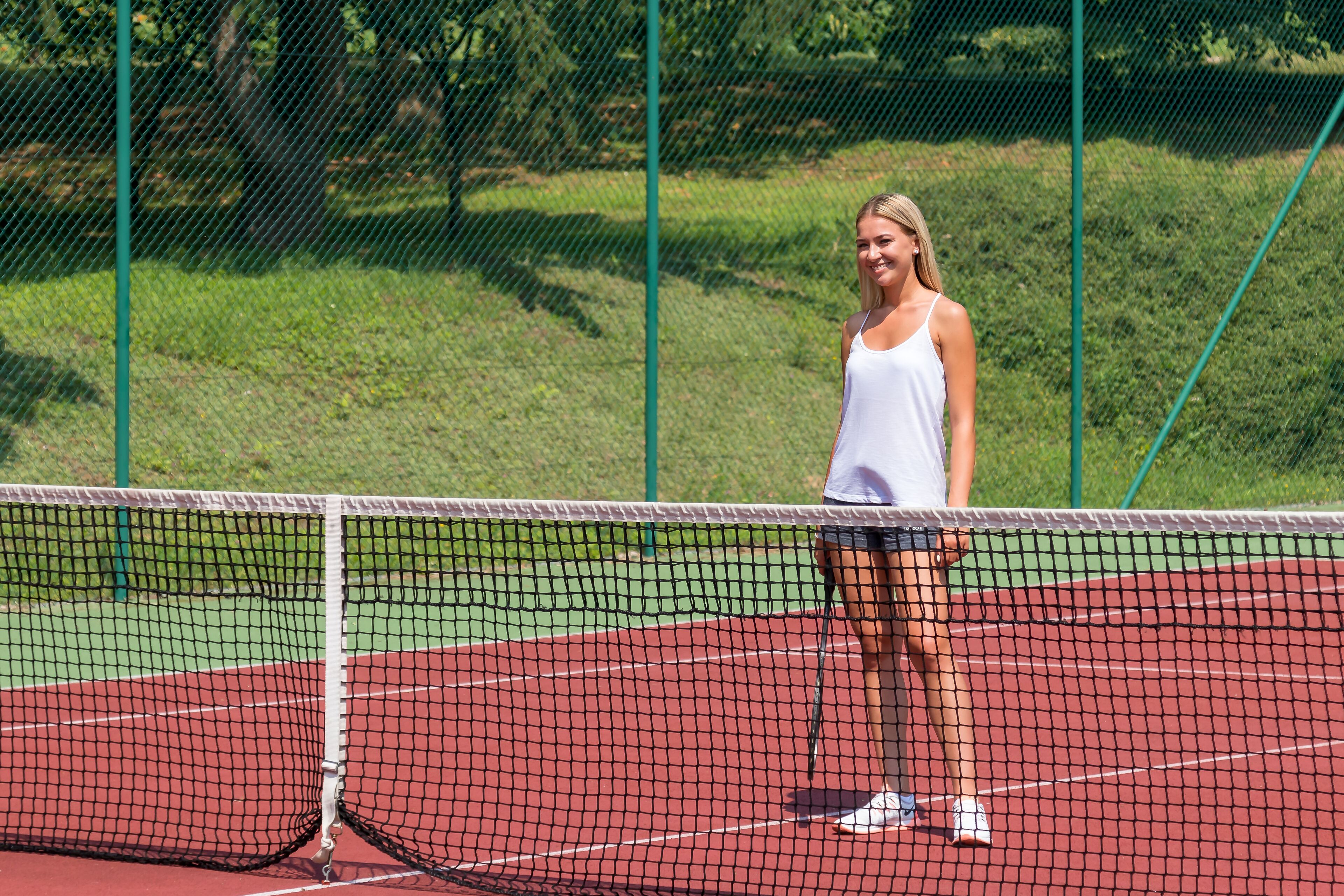 A tennis court with a net in the foreground and a grassy area in the background.
