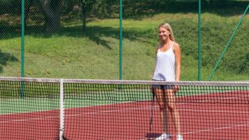 Un court de tennis avec un filet au premier plan et une zone herbeuse en arrière-plan.