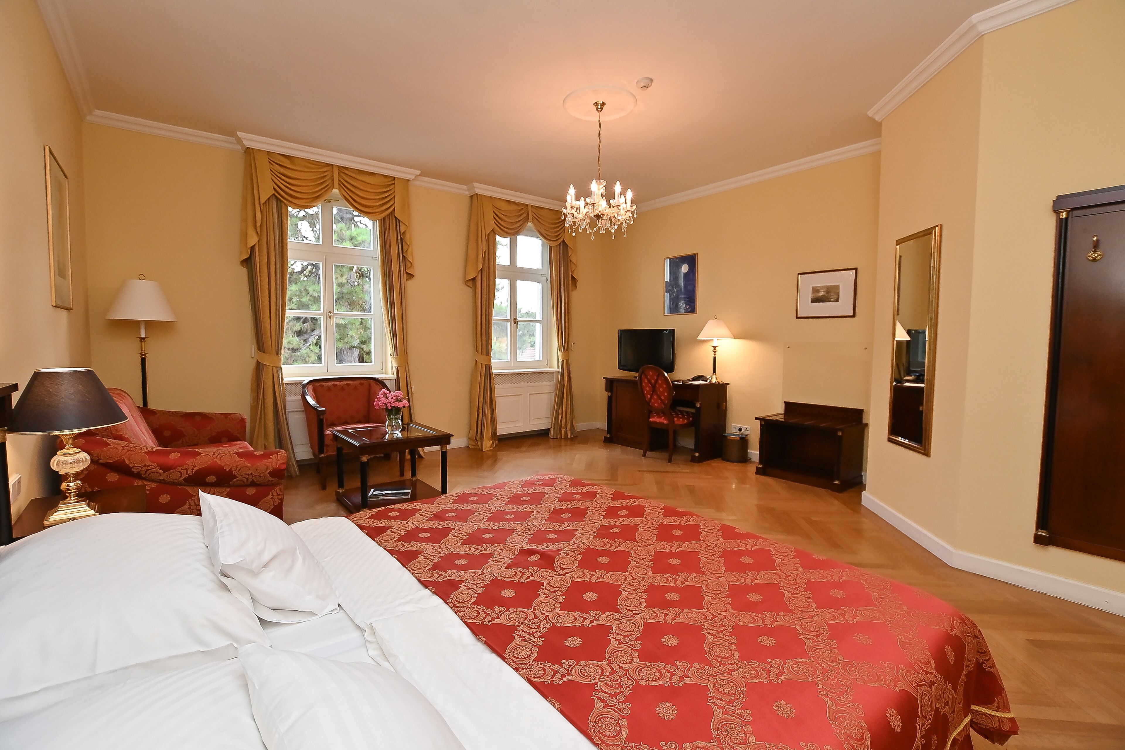 A hotel room with a large bed, a desk, a chair, a TV, and a wardrobe.