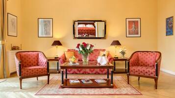 Une pièce comprenant deux fauteuils rouges, une table basse en bois avec des livres, un vase de fleurs et un lit recouvert d’une couvre-lit à motifs rouges et blancs.