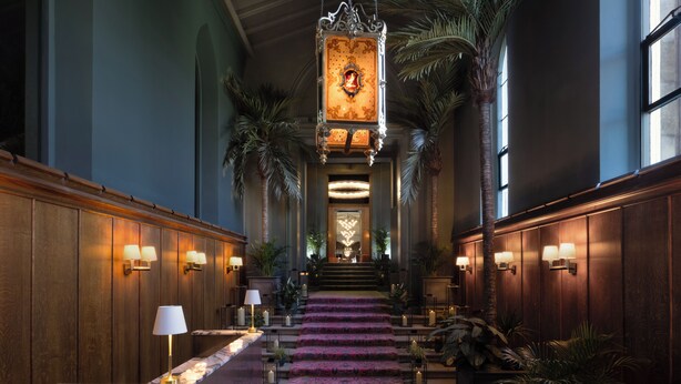 A grand hotel lobby with a marble reception desk, a staircase with a patterned carpet, and wall-mounted lighting. - JA Mar Hall Scotland (Bishopton)