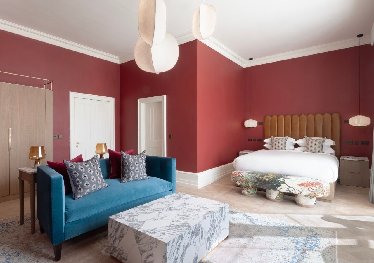 Une chambre avec un canapé bleu, un lit recouvert d’une literie à motifs floraux et une table basse en marbre.