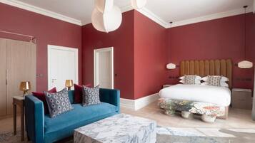 Une chambre avec un canapé bleu, un lit recouvert d’une literie à motifs floraux et une table basse en marbre.