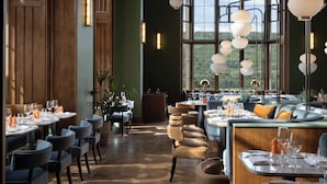 A restaurant with high wooden walls, large windows, and multiple dining tables set with white tablecloths and chairs. - JA Mar Hall Scotland (Bishopton)