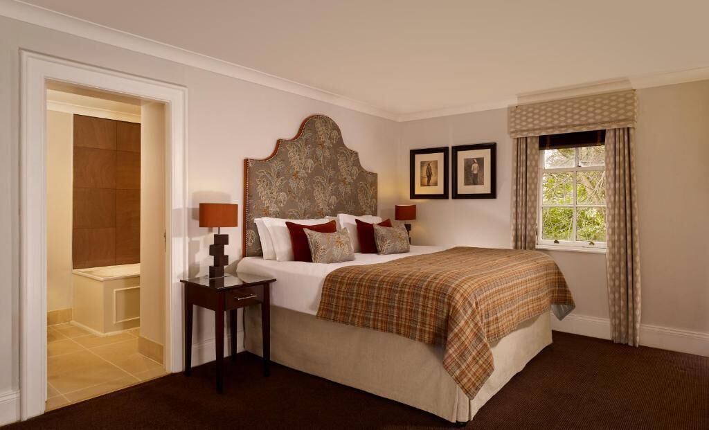 Une chambre à coucher avec un grand lit, deux tables de chevet avec des lampes, une tête de lit et une fenêtre avec des rideaux.