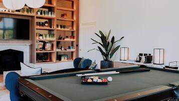 Una mesa de billar con taco, una estantería y un televisor en un moderno salón.
