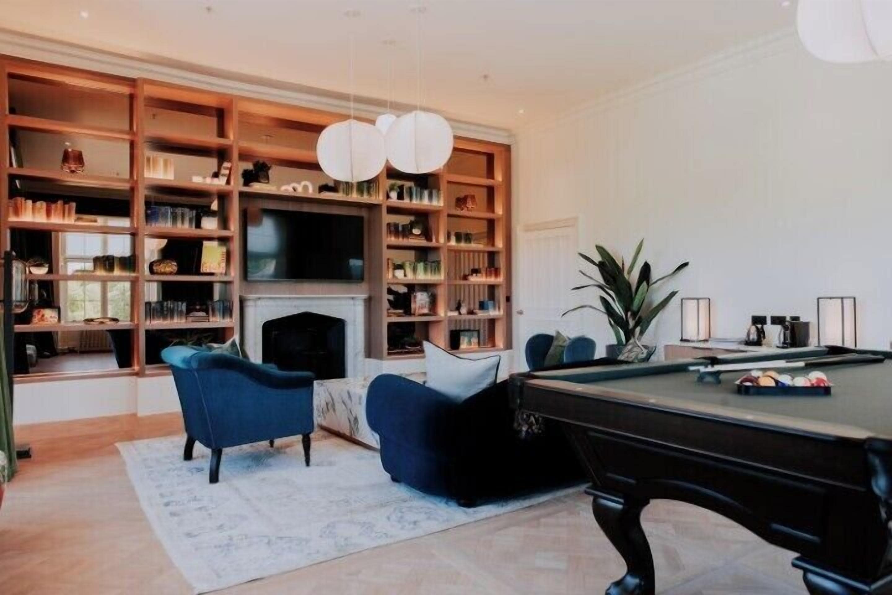 A living room with a pool table, blue sofas, a fireplace, and a large bookshelf.