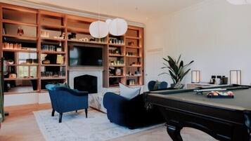 A living room with a pool table, blue sofas, a fireplace, and a large bookshelf.