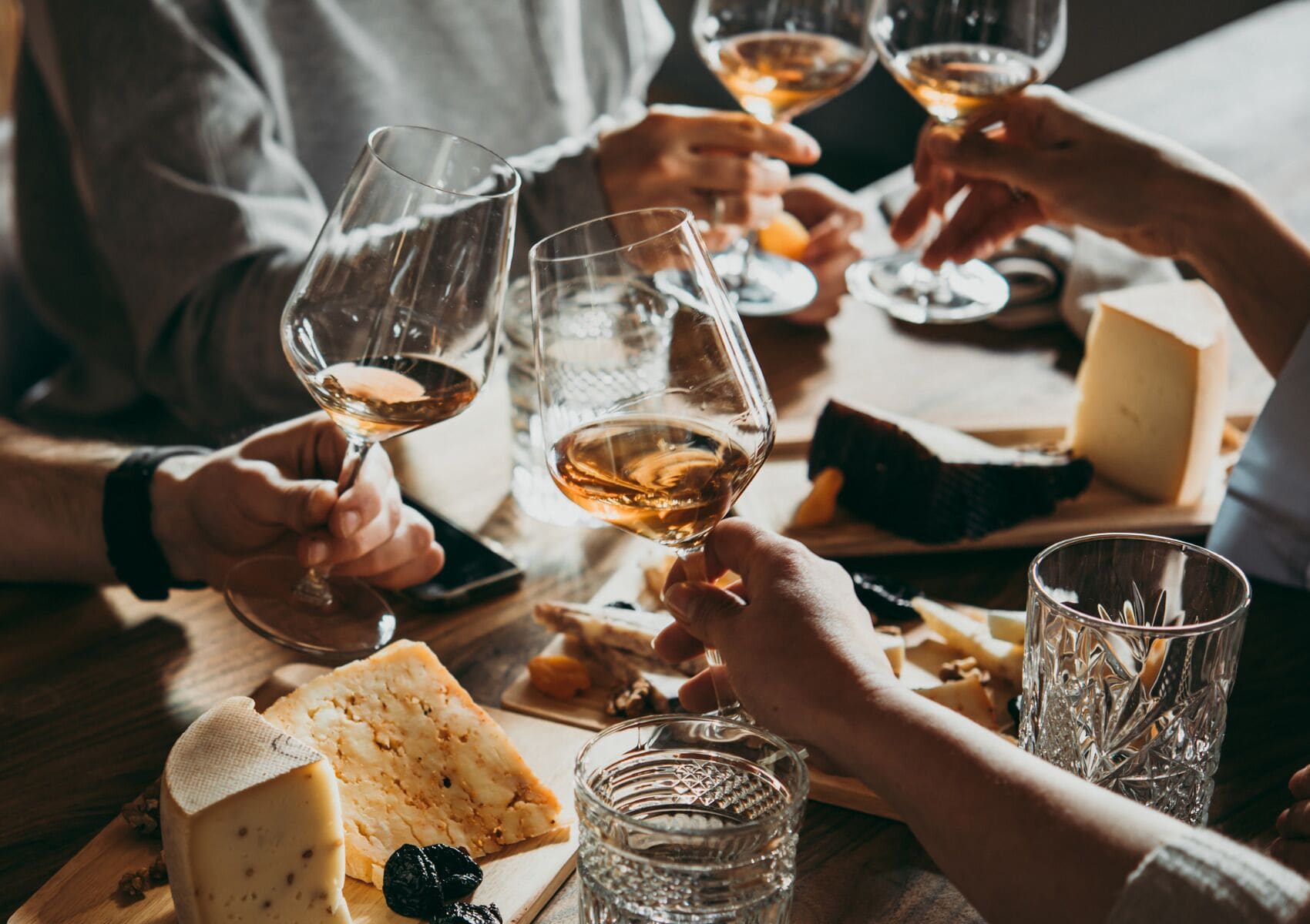 Een groep mensen die met wijnglazen proosten aan een tafel met kaas en crackers.