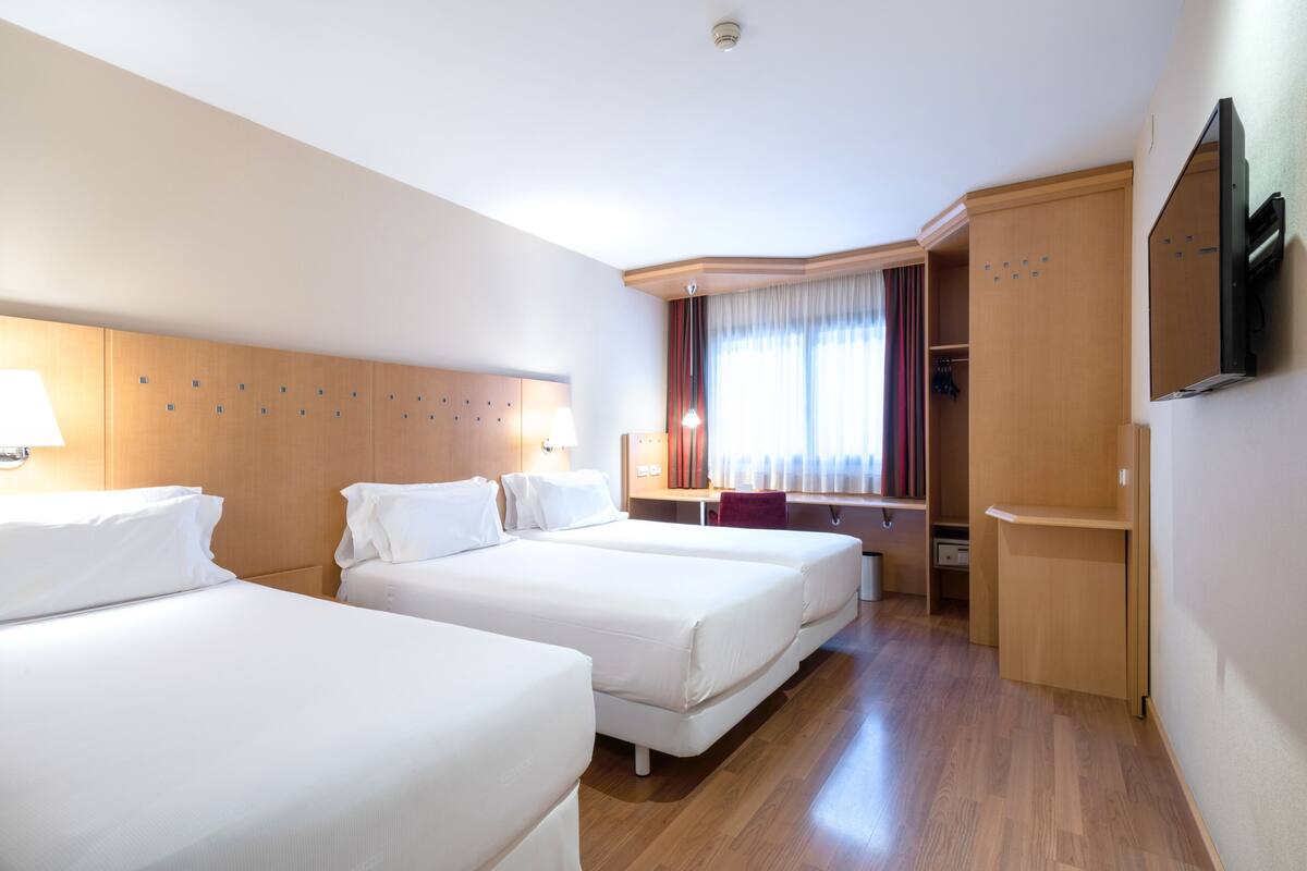 Une chambre d’hôtel avec deux lits, un bureau, une armoire et un téléviseur.