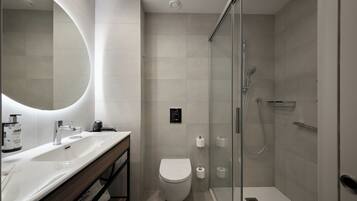 Un baño moderno con ducha de vidrio, lavamanos blanco y retrete.