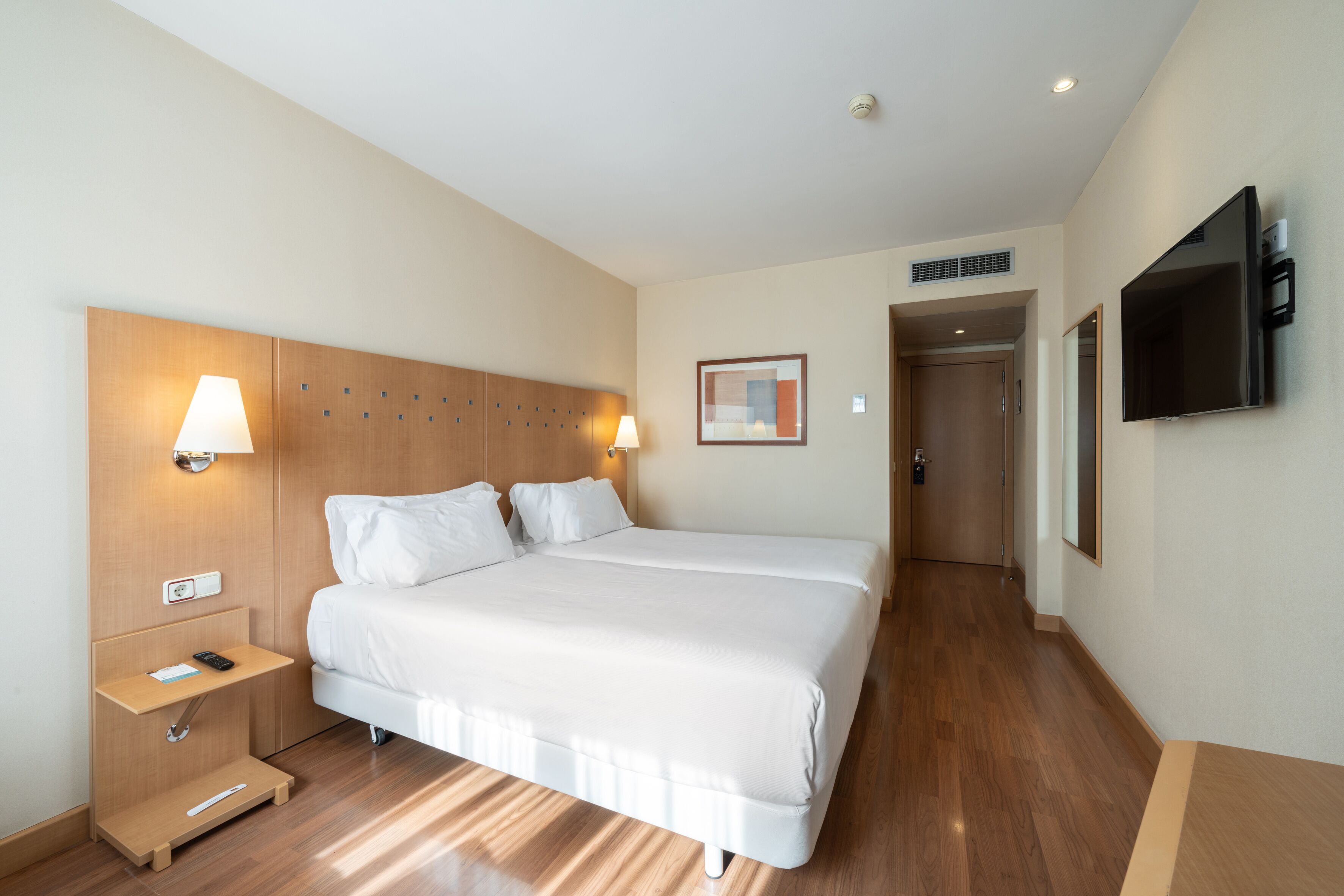 Une chambre d’hôtel avec un grand lit, des tables de chevet, une télévision et une porte donnant sur une autre pièce.