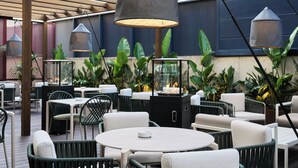 Un espace extérieur aménagé en terrasse, avec des tables et des chaises rondes, un meuble noir et des lampes suspendues.