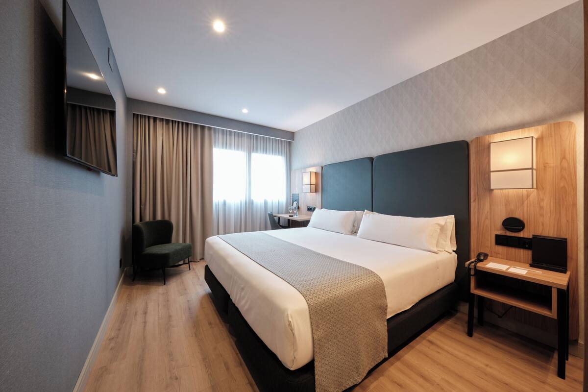 Une chambre d’hôtel moderne, dotée d’un grand lit, d’un bureau, d’une chaise et d’un téléviseur fixé au mur.