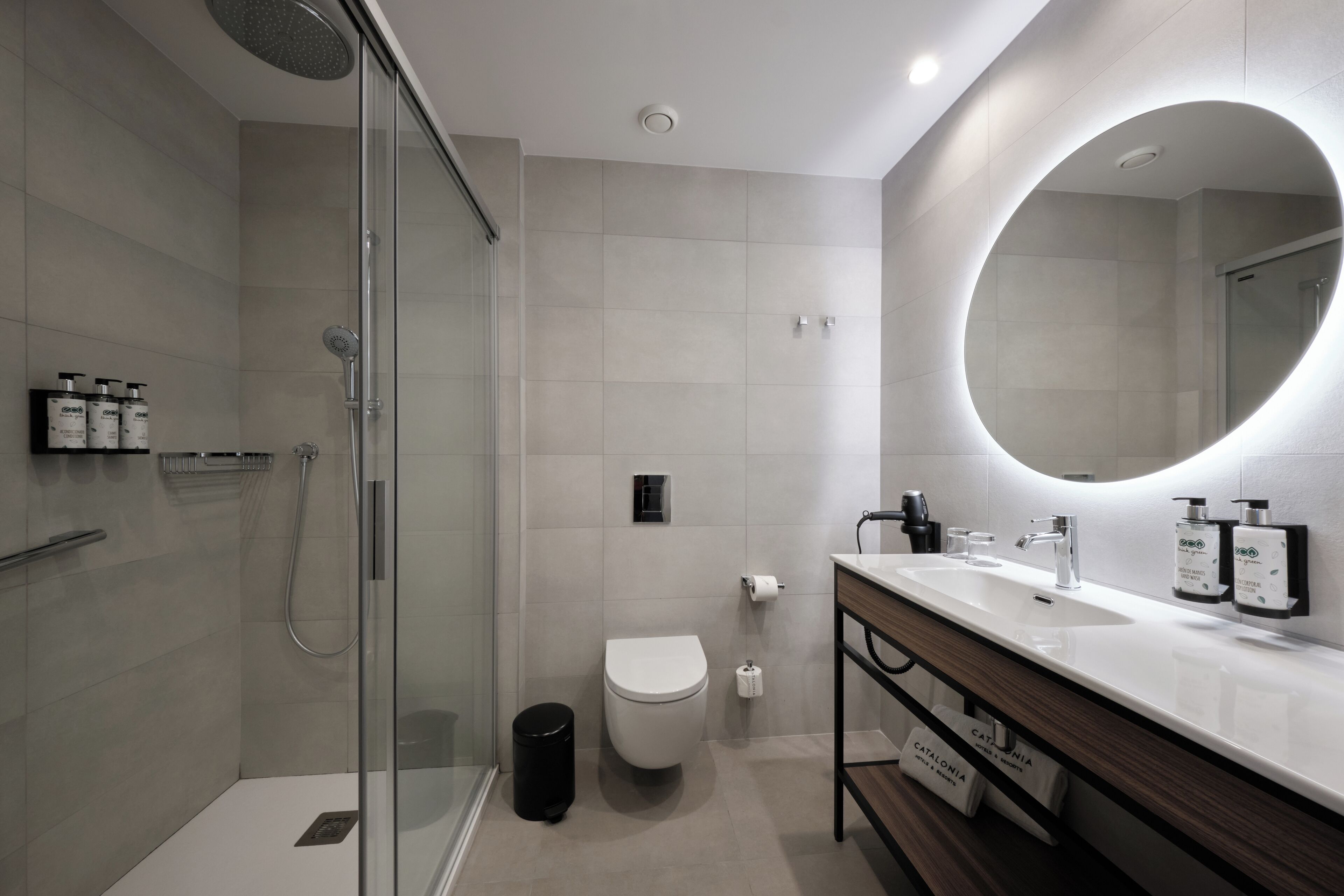 Een moderne badkamer met een douchecabine van glas, een wit toilet en een wastafel met een grote spiegel.