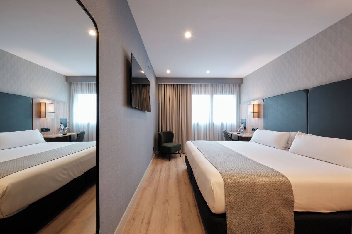Une chambre d’hôtel moderne équipée de deux lits, d’un bureau, d’une chaise, d’une télévision et d’un grand miroir.
