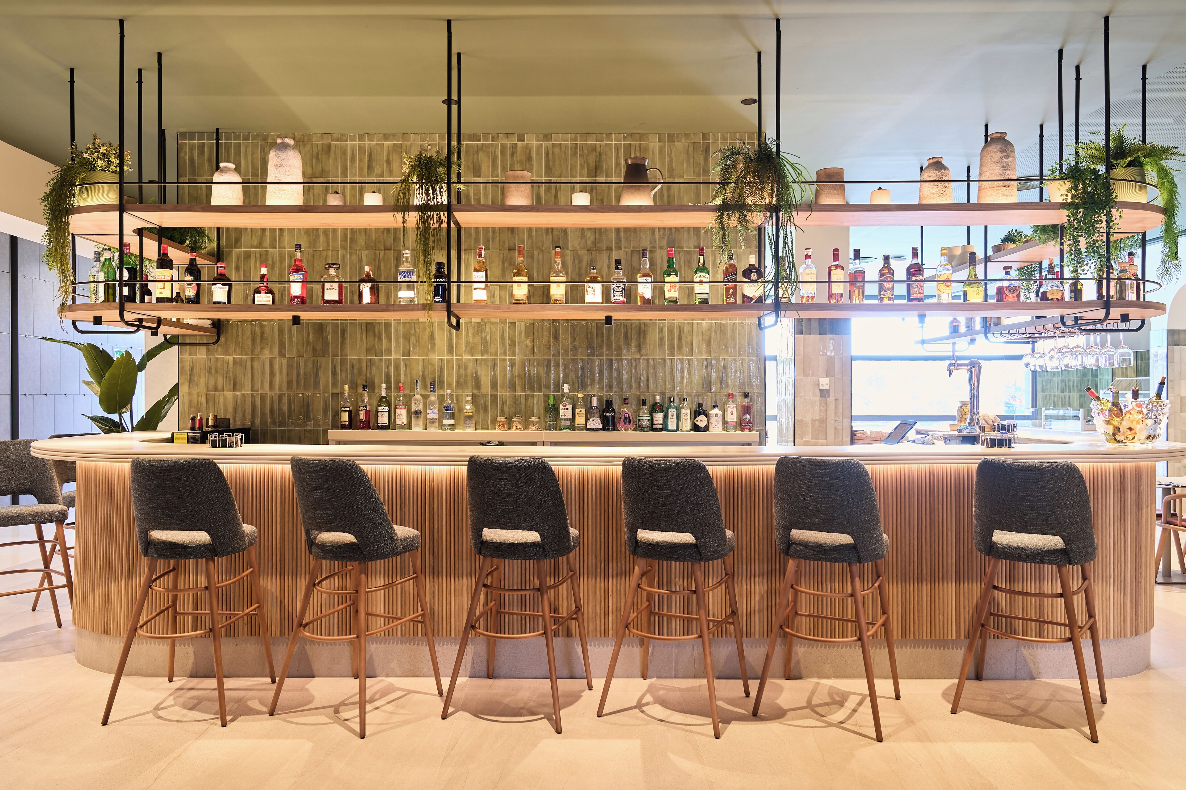 Una zona de bar con mostrador de madera, varias estanterías llenas de botellas y varios taburetes.