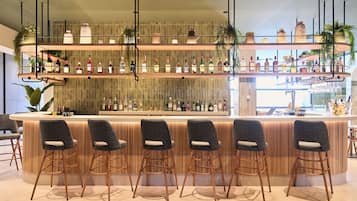 Una zona de bar con mostrador de madera, varias estanterías llenas de botellas y varios taburetes.