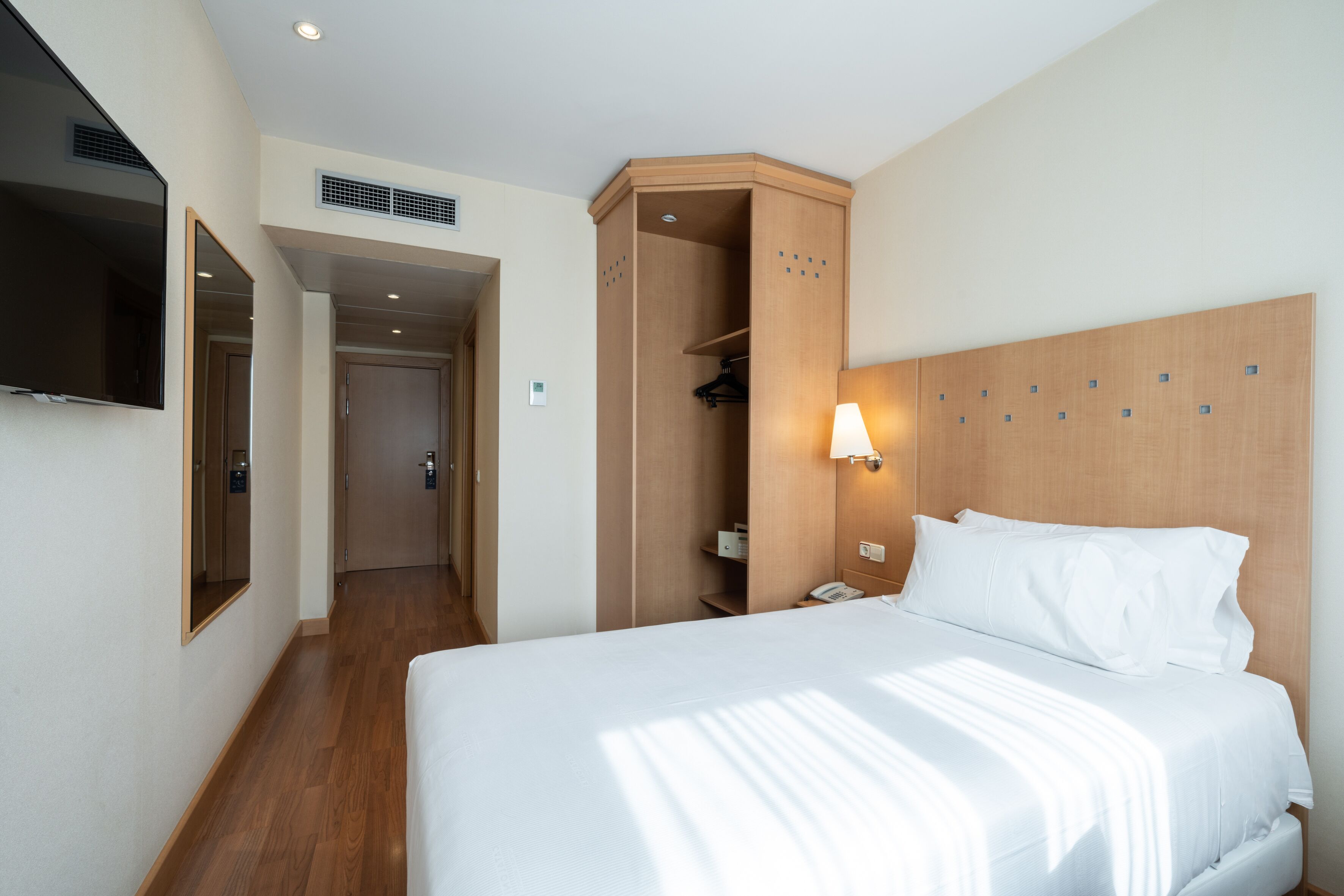 Una habitación de hotel con una cama grande, un armario, un espejo y un televisor en la pared.