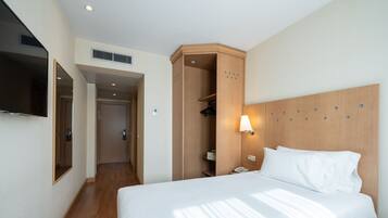 Una habitación de hotel con una cama grande, un armario, un espejo y un televisor en la pared.