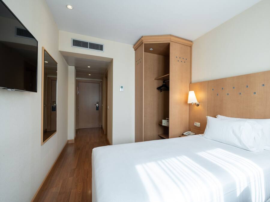 Una habitación de hotel con una cama grande, un armario, un espejo y un televisor en la pared.