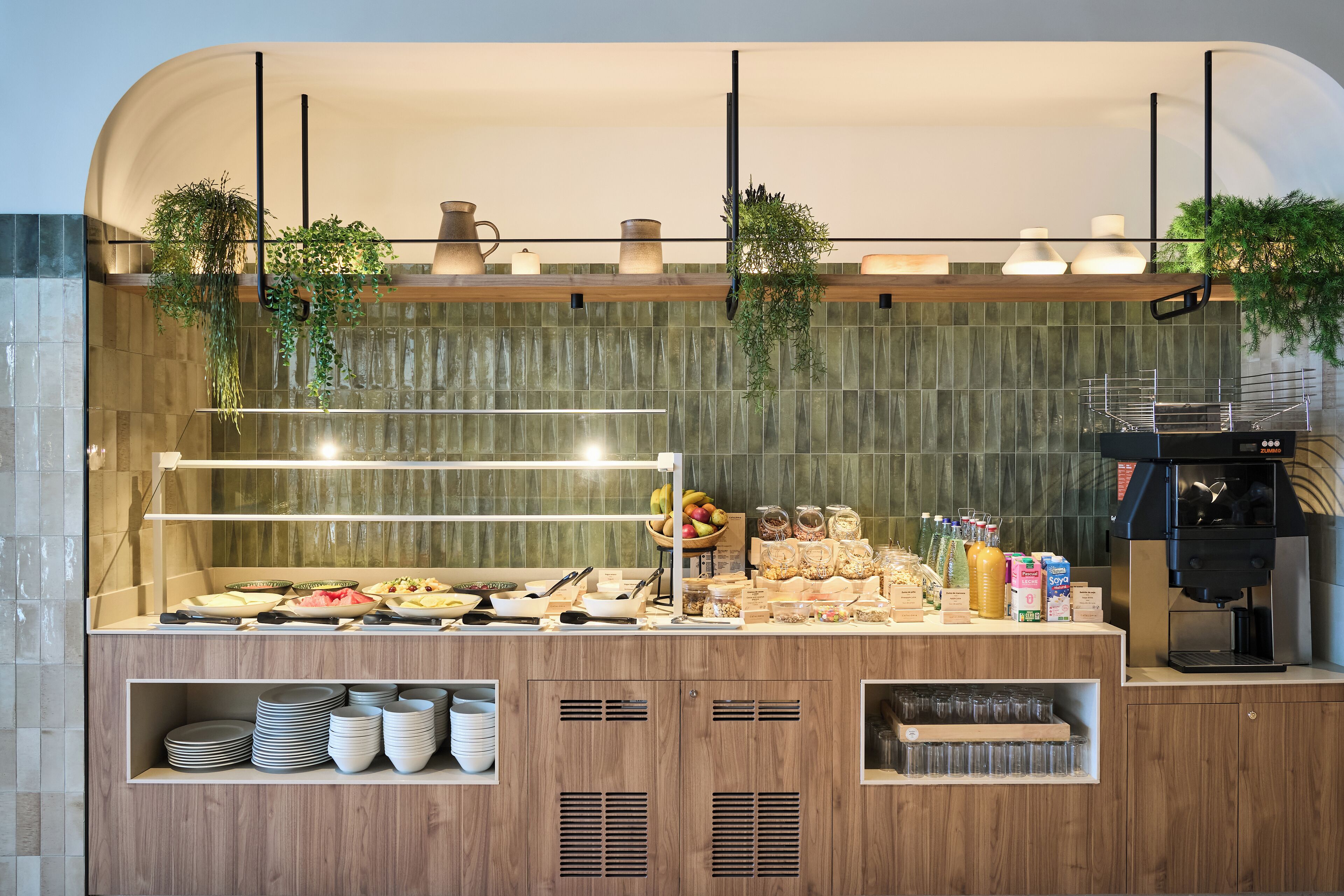 A buffet setup with various food items, a coffee machine, and hanging plants.