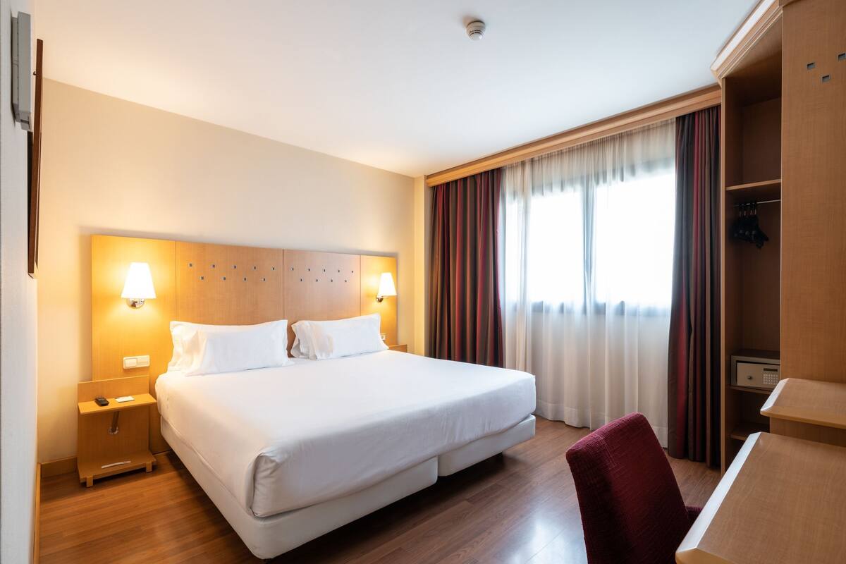 Une chambre d’hôtel avec un grand lit, des lampes de chevet, une tête de lit en bois, un bureau et une armoire.