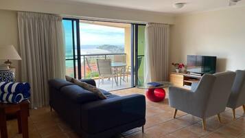 Een moderne woonkamer met een bank, fauteuils, een televisie en een balkon met uitzicht.